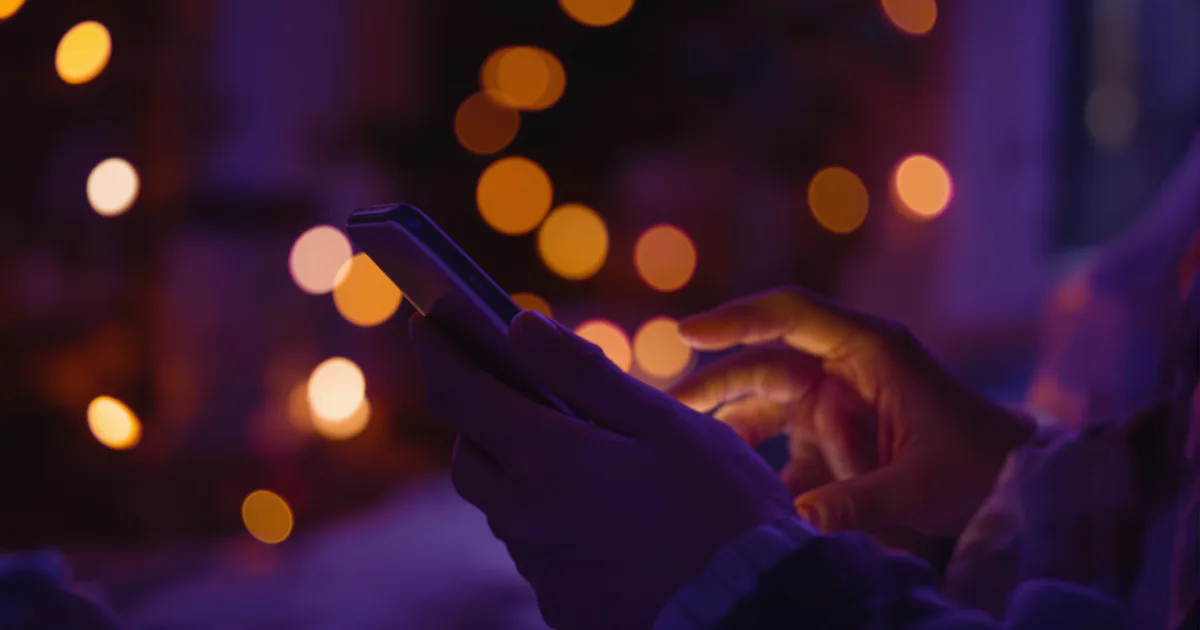 Hands holding a phone starting a new chat in a cozy room lit by warm bokeh at dusk